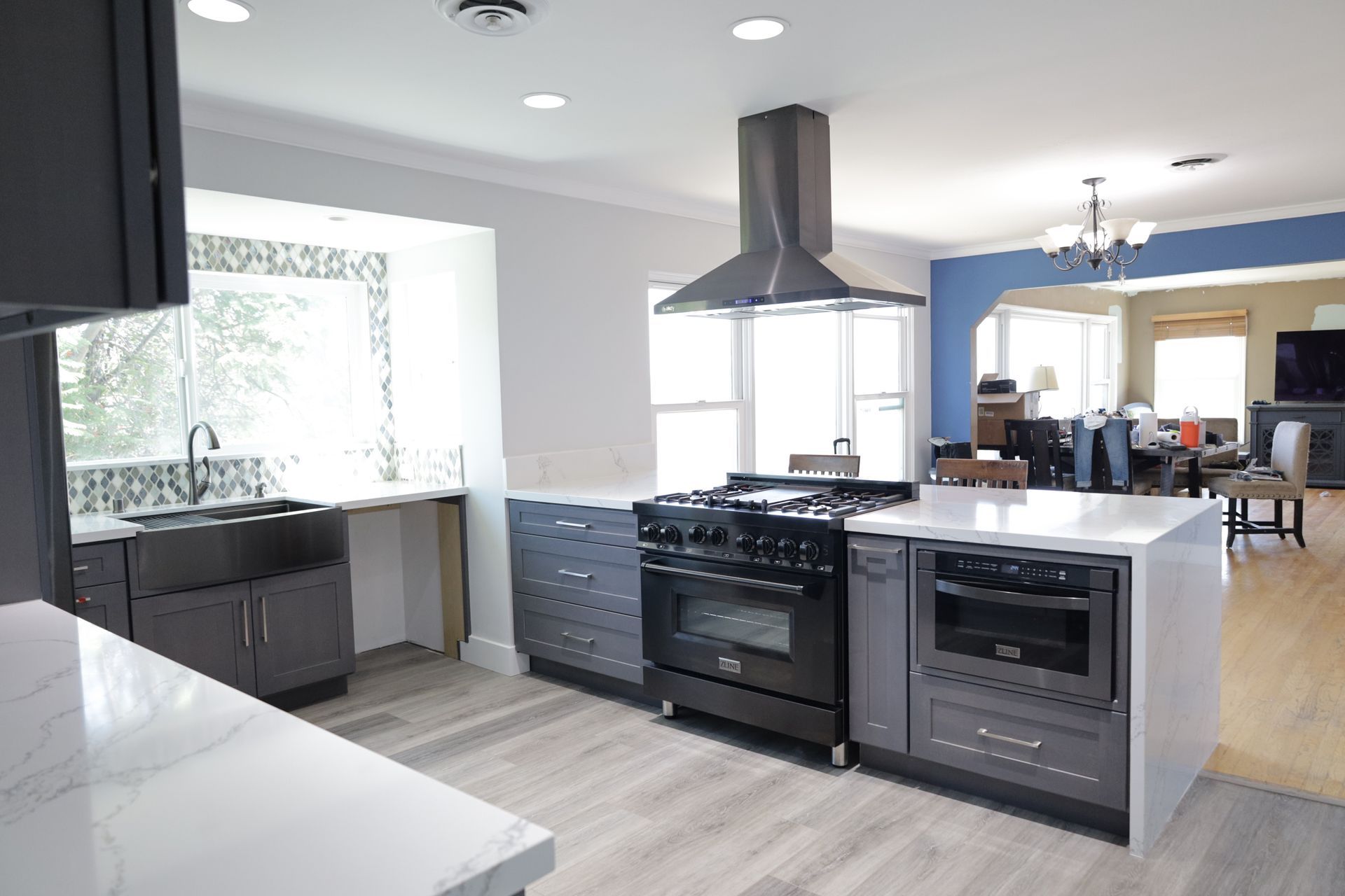 Modern kitchen with black stove, stainless appliances, white counters, and open dining area beyond