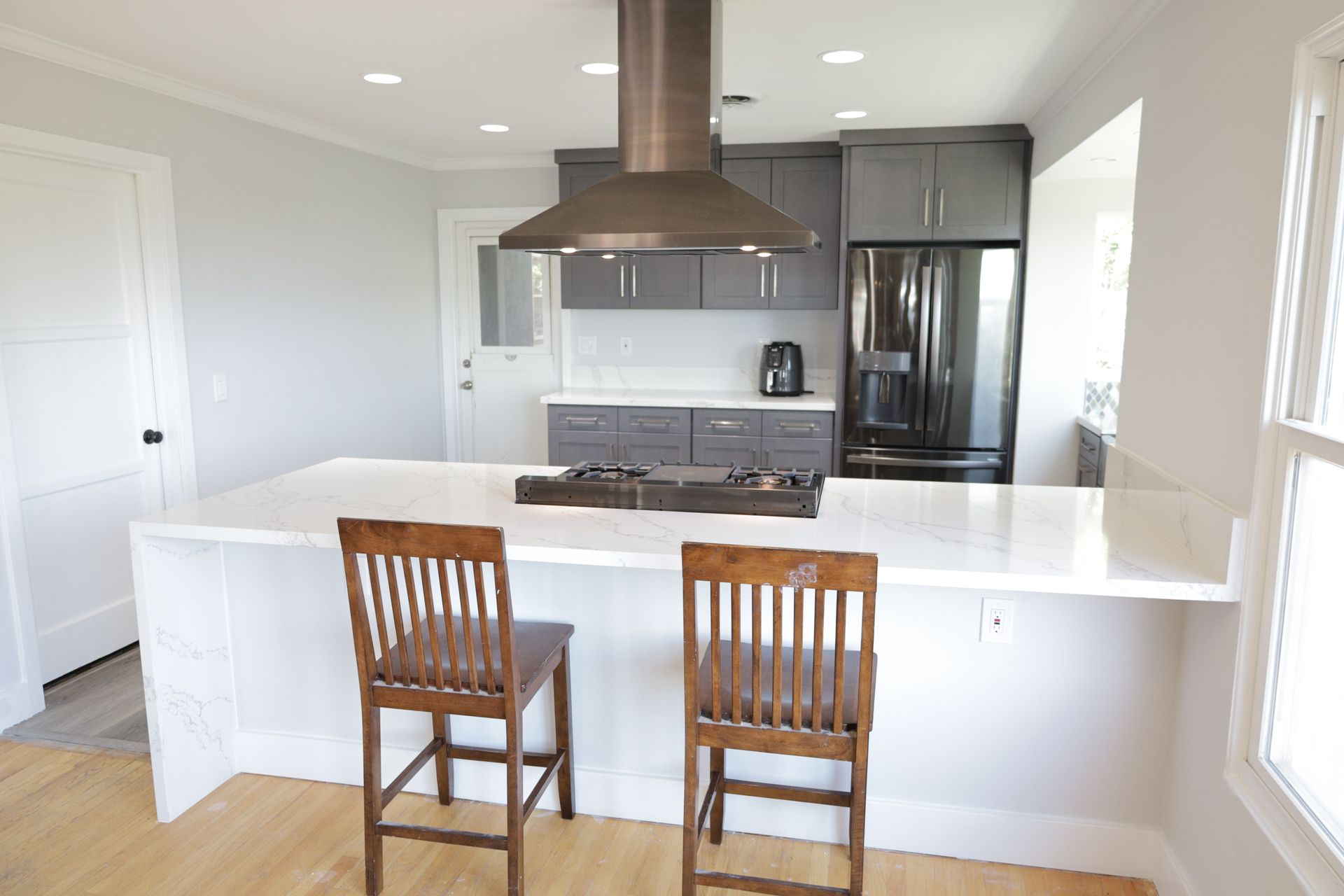 Modern kitchen with white island, two wooden stools, and stainless steel appliances.