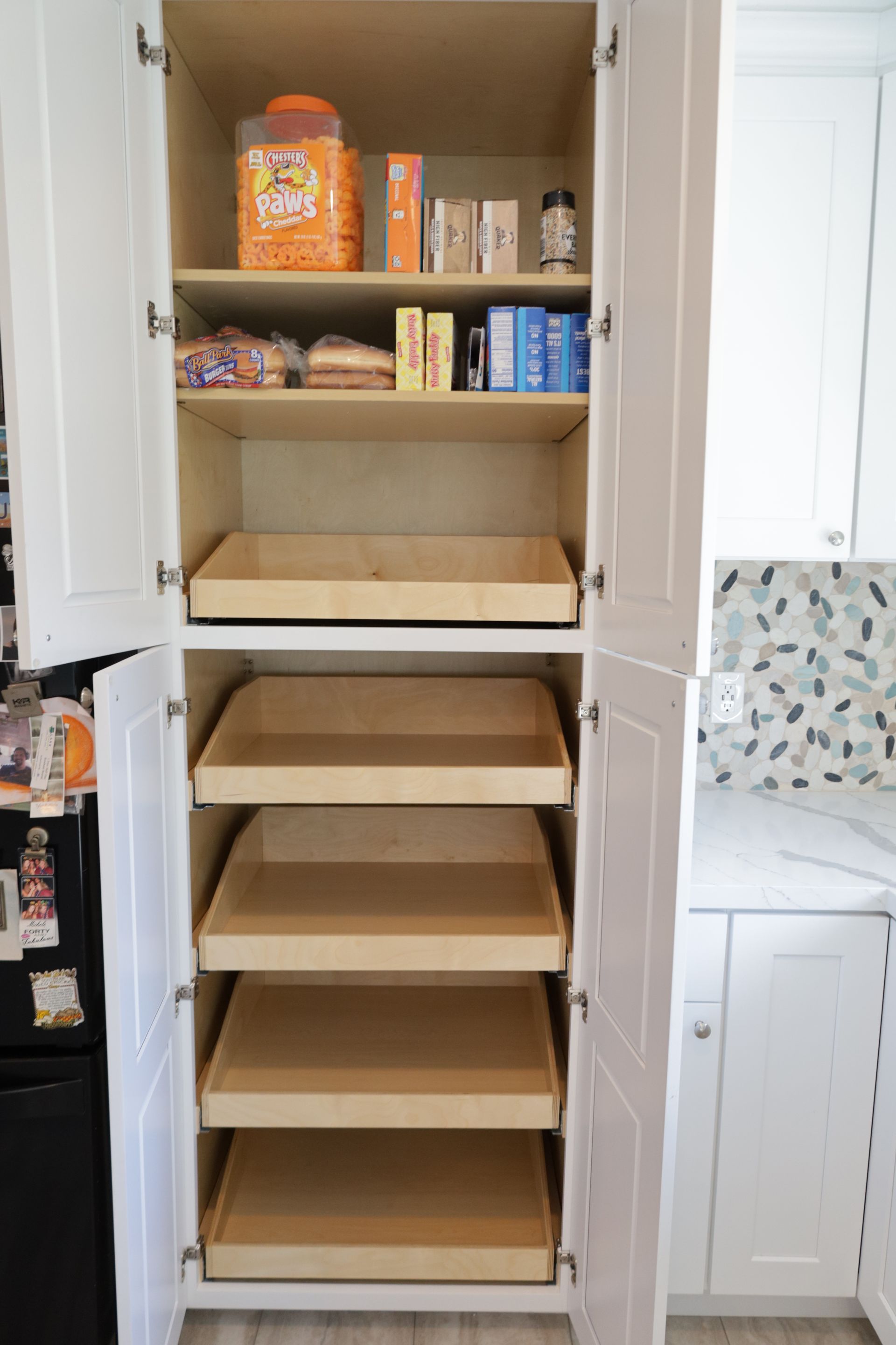 Open pantry cabinet with pull-out shelves, mostly empty, holding a few cereal boxes and canned goods.