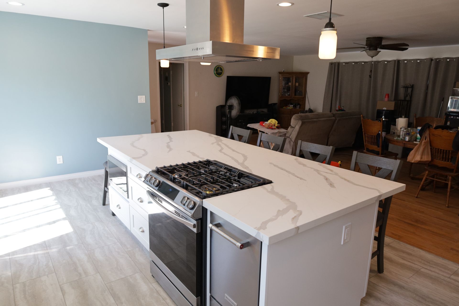 Modern kitchen with white island, gas cooktop, stainless oven, and dining area in the background
