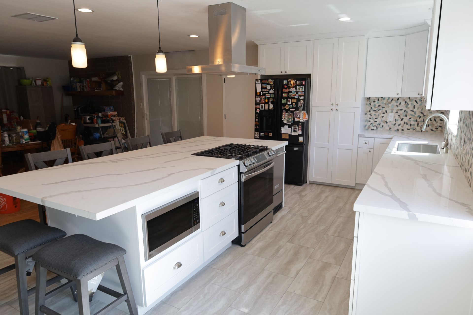 Bright modern kitchen with white island, black stools, stainless appliances, and light wood floors
