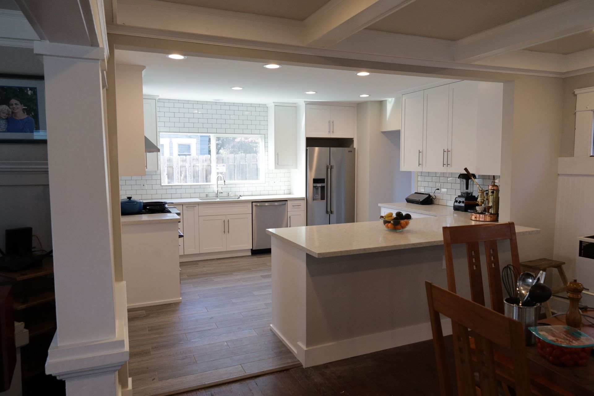 Bright kitchen with white cabinets, island, and stainless steel refrigerator in an open dining area.