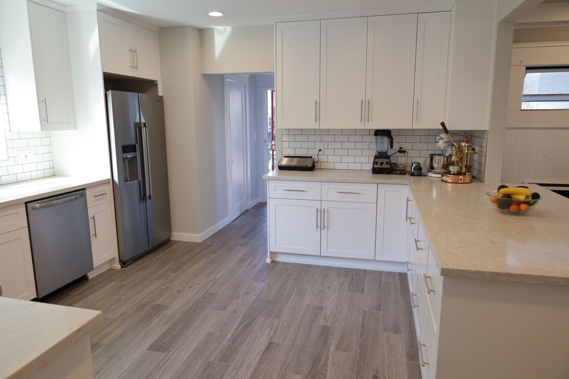 Bright modern kitchen with white cabinets, stainless fridge, gray floors, and light countertops