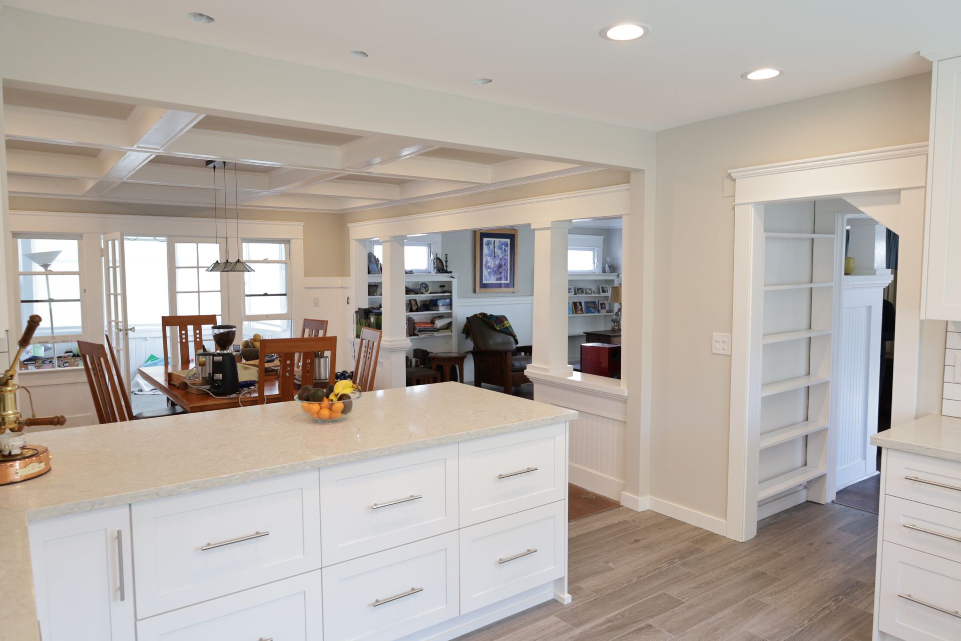 Bright white kitchen with island, open doorway, and dining area in the background