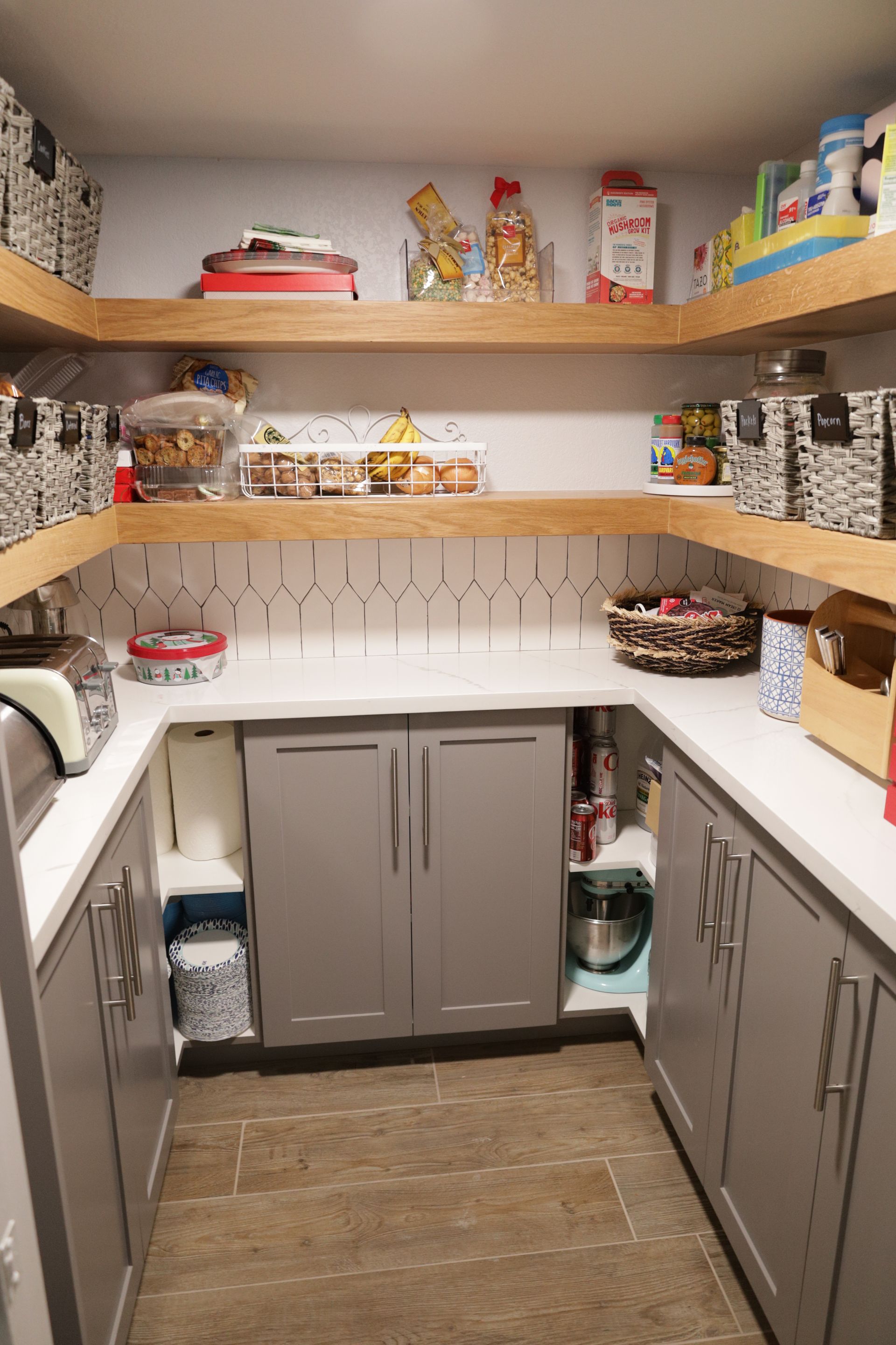 Pantry closet with gray cabinets, white shelves, and neatly stored food and supplies.