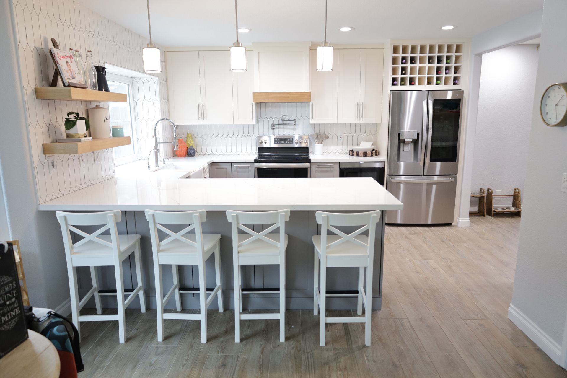 Bright white kitchen with island, five stools, stainless fridge, and pendant lights
