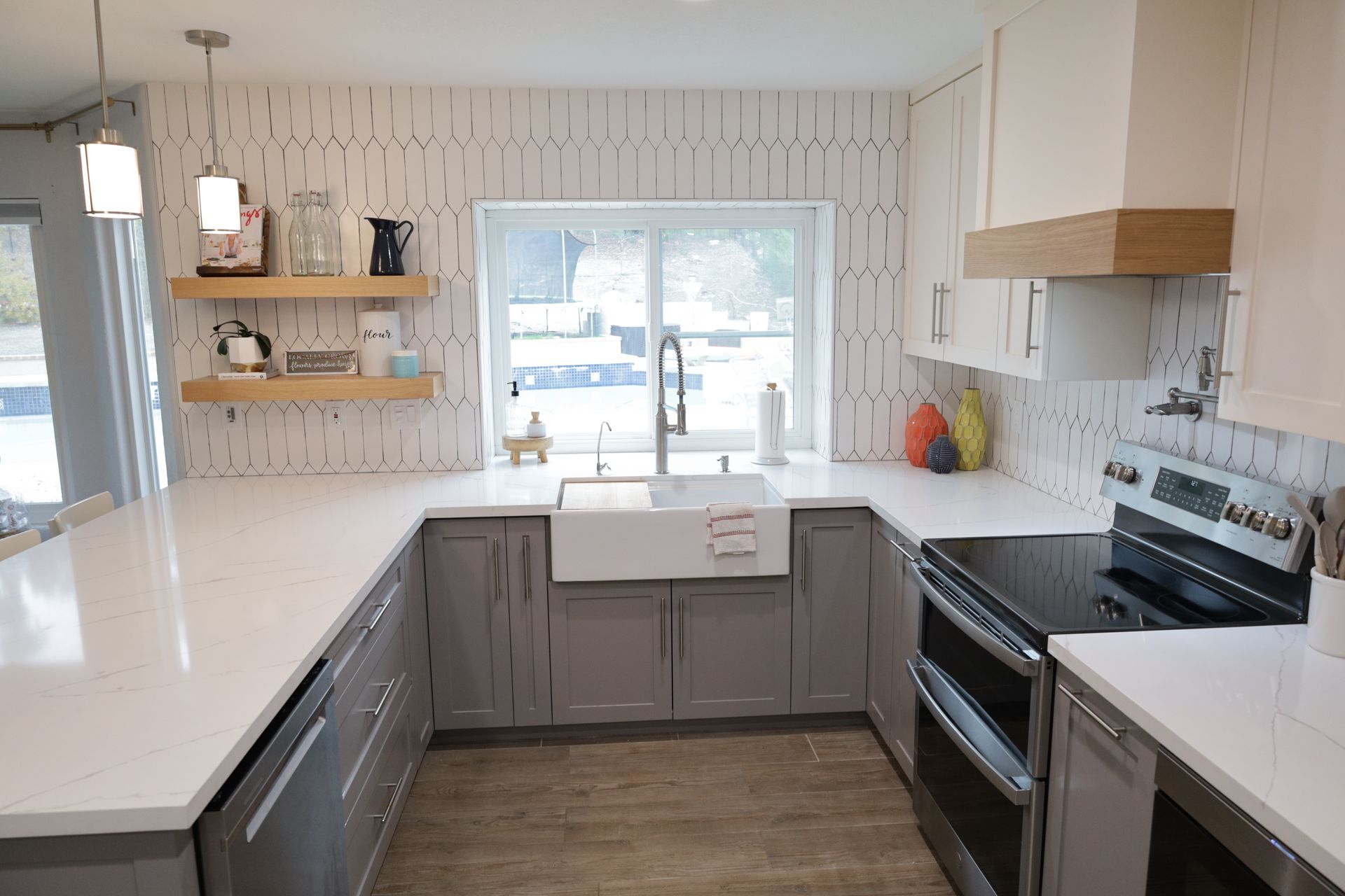 Bright modern kitchen with white countertops, gray cabinets, black stove, and a farmhouse sink by a window