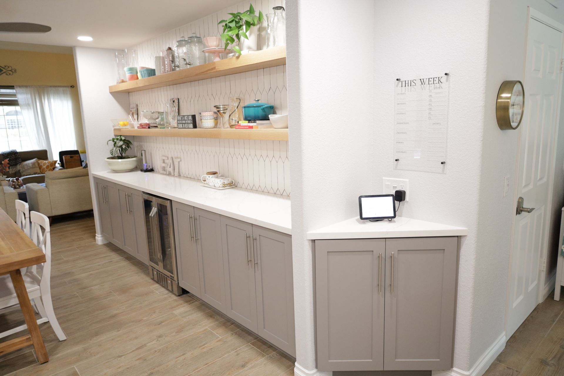 Bright kitchen with open shelves, long counter, cabinets, and a small table near a doorway