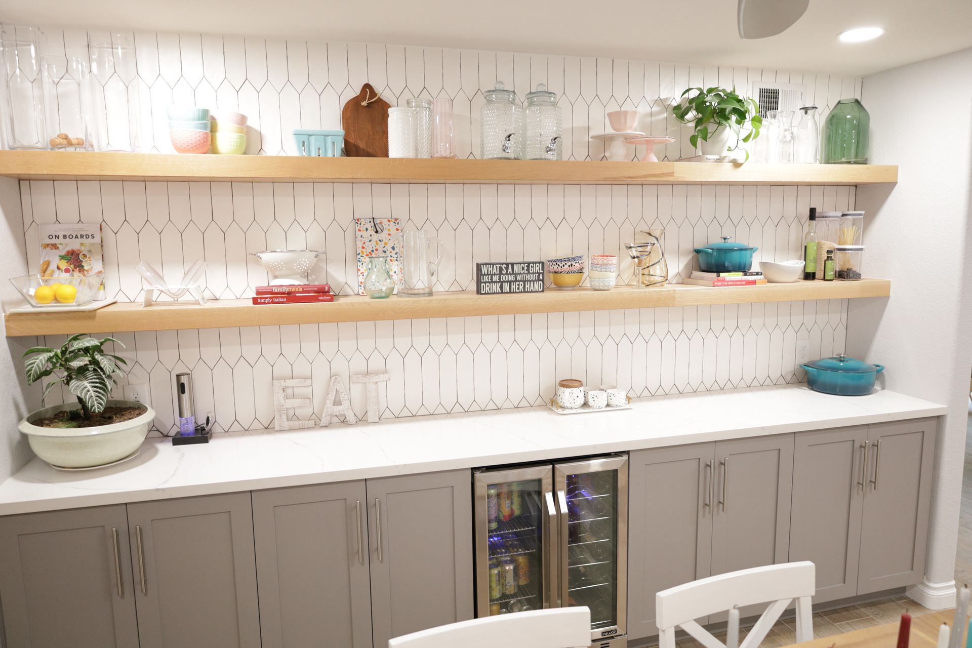 Modern kitchen with open shelves, gray cabinets, white countertop, and potted plants.