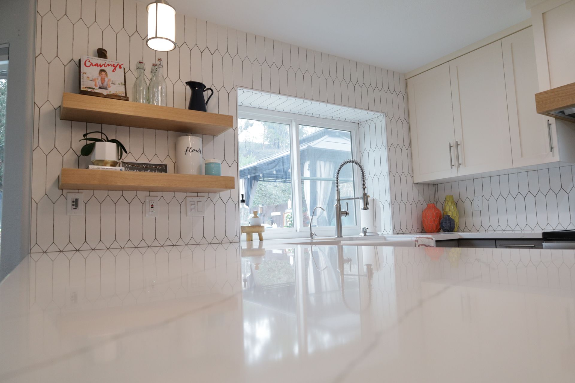 Bright modern kitchen with white countertops, open wooden shelves, and a window over the sink
