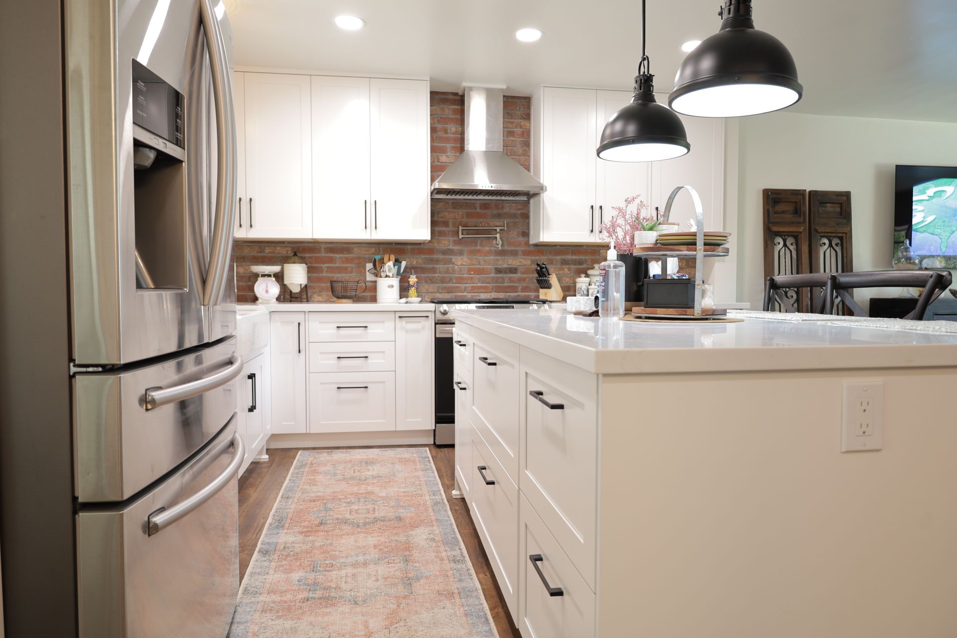 Modern white kitchen with island, stainless steel appliances, brick backsplash, and pendant lights