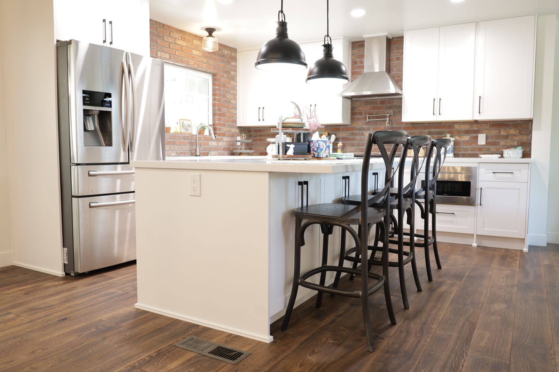 Bright modern kitchen with white cabinets, stainless fridge, island, and dark bar stools on wood floors