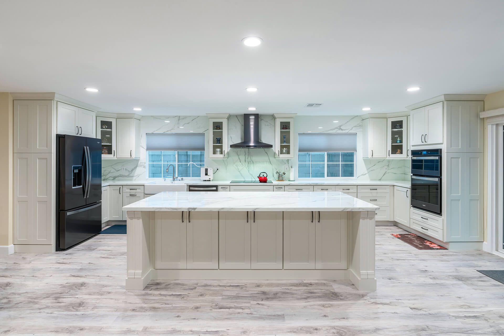 Bright modern white kitchen with large island, black appliances, and light wood floors