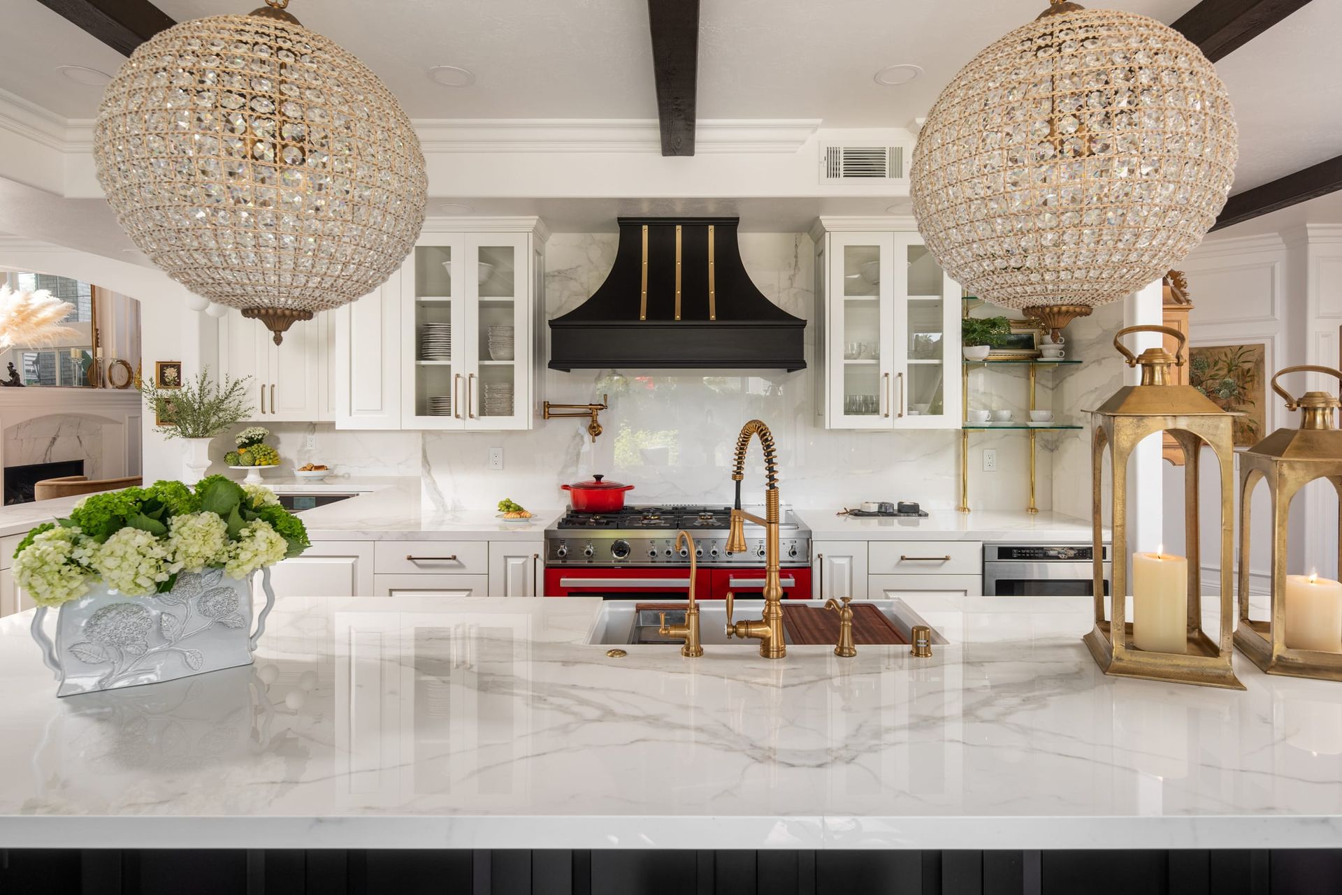 Bright white kitchen with marble island, gold fixtures, beaded chandeliers, and black range hood
