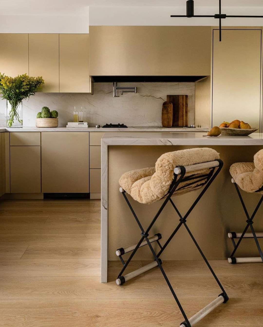 Modern beige kitchen with island, tan stools, and a potted plant on the counter