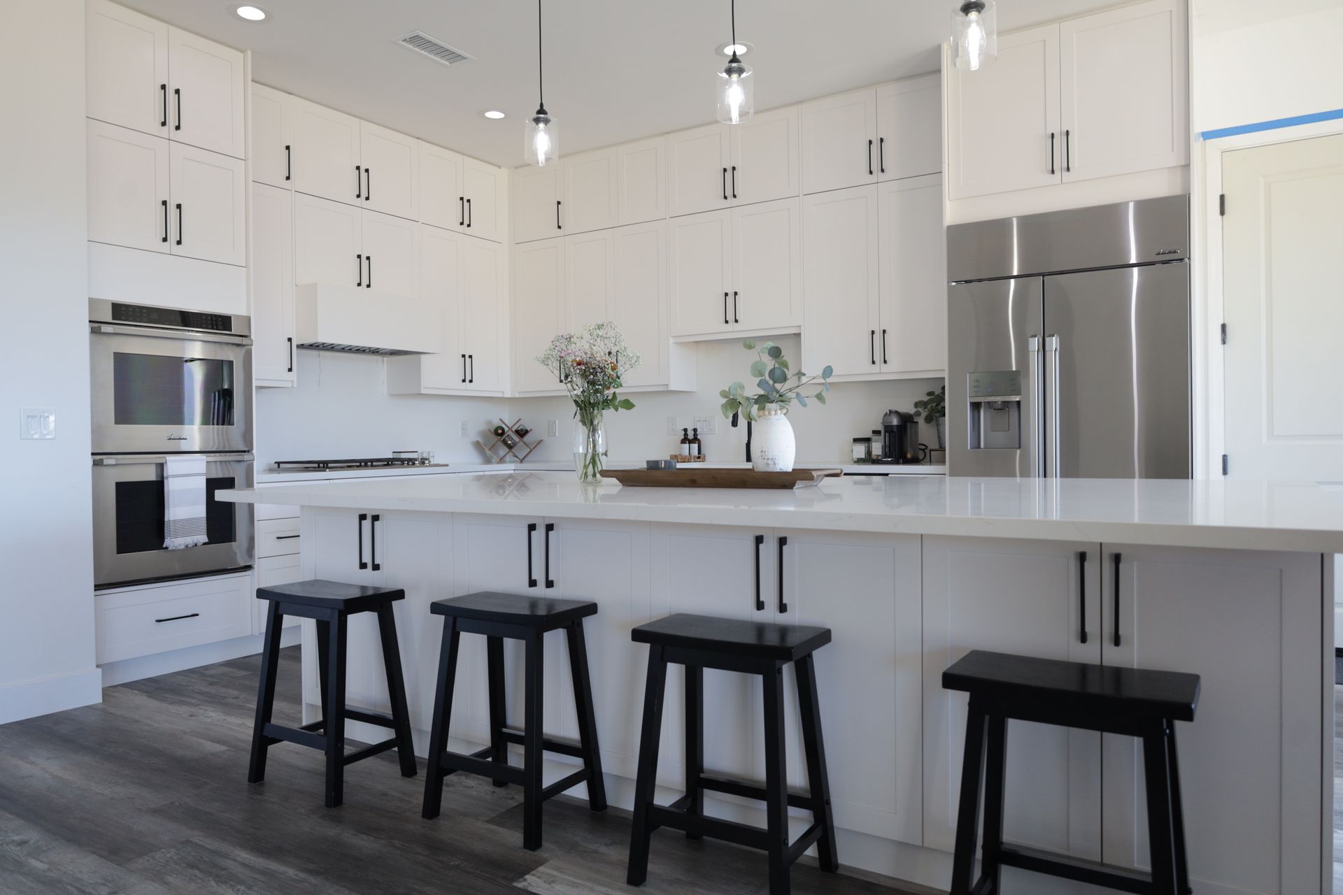 Modern white kitchen with island, stainless steel appliances, and four black stools