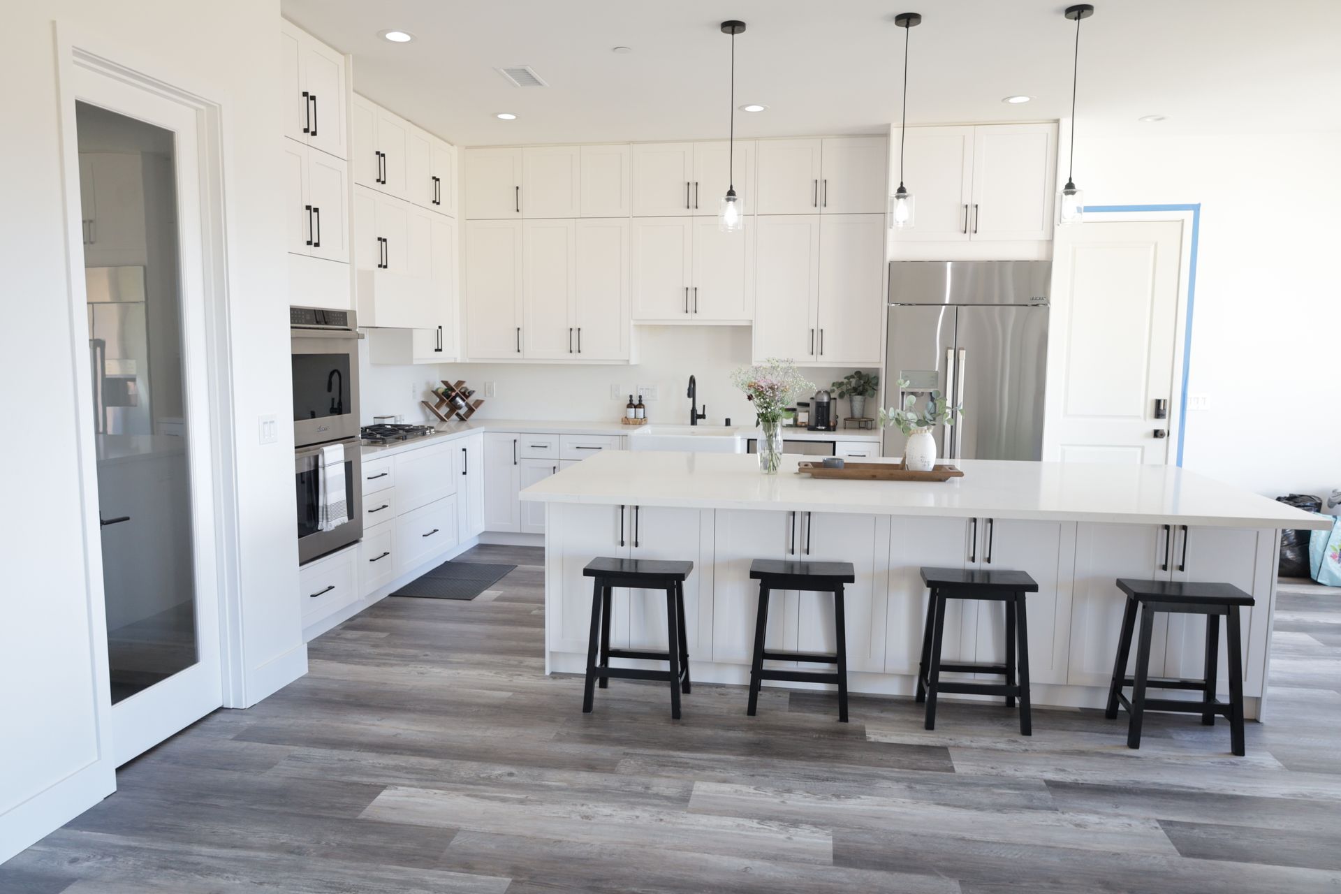 Bright white modern kitchen with island, four stools, stainless fridge, and gray wood-look floor