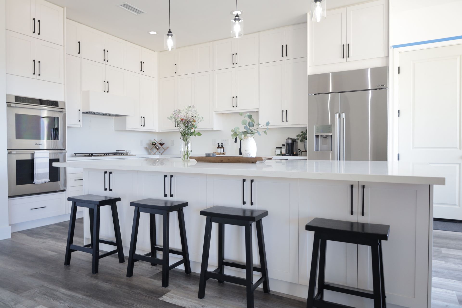 Bright modern white kitchen with island, black stools, stainless steel appliances, and pendant lights