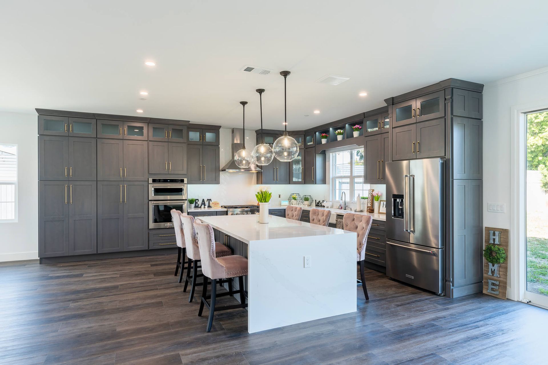Modern gray kitchen with island, pendant lights, barstools, stainless appliances, and hardwood floors