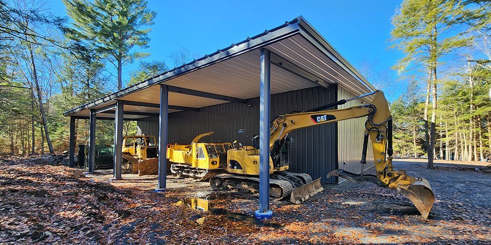 Yellow excavator under a metal-roofed shed in a wooded rural lot