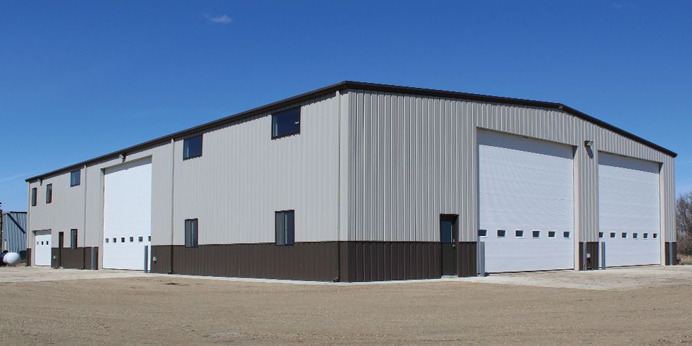 Large gray metal warehouse with multiple garage doors under a clear blue sky