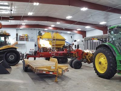 Farm equipment in a warehouse, including a green tractor, red machinery, and trailers.