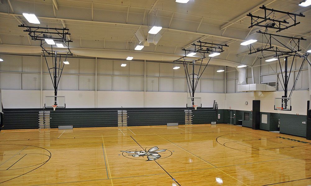 Empty indoor basketball gym with polished wood floor, hoops, and wall-mounted backboards