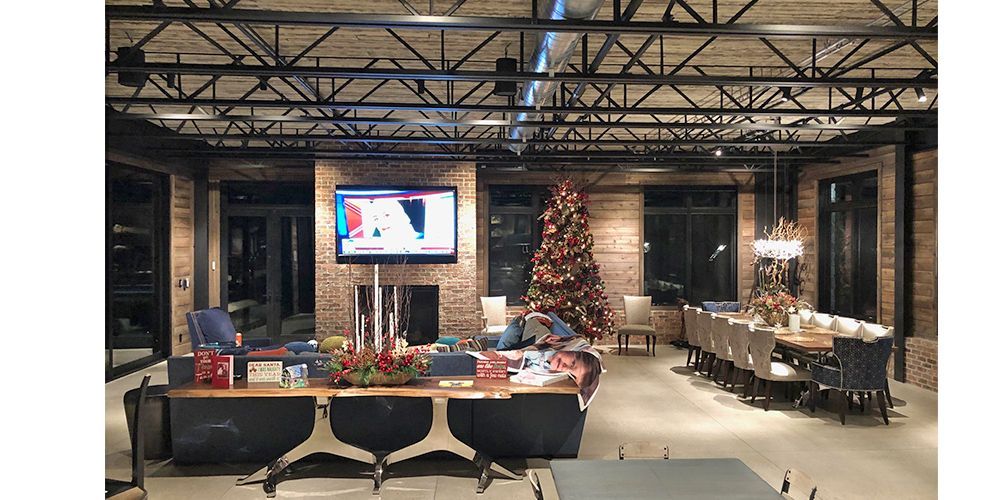 Festive dining hall with a decorated Christmas tree, long table settings, and a TV on a brick wall