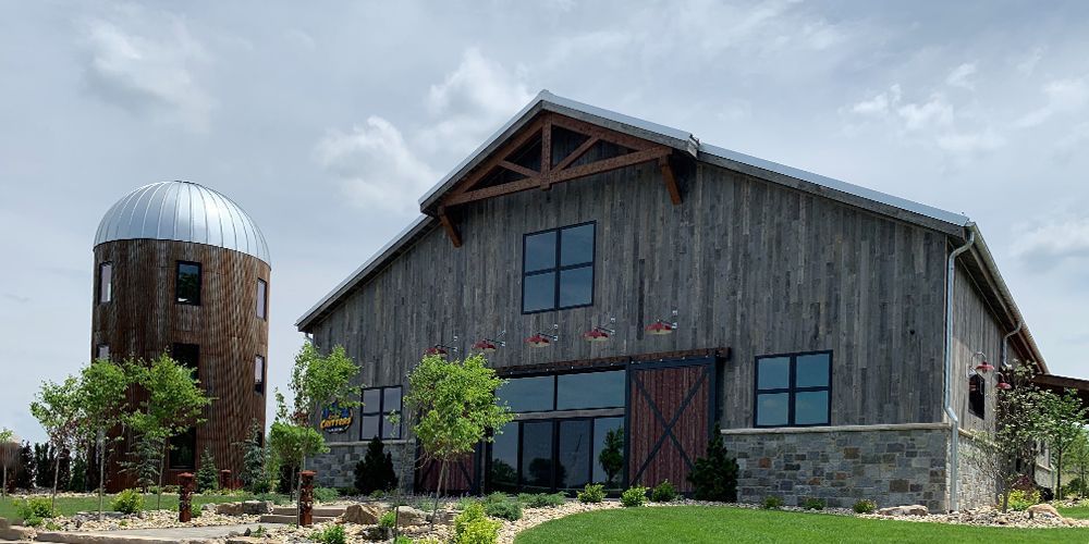 Rustic gray barn-style building beside a round metal silo under a blue sky