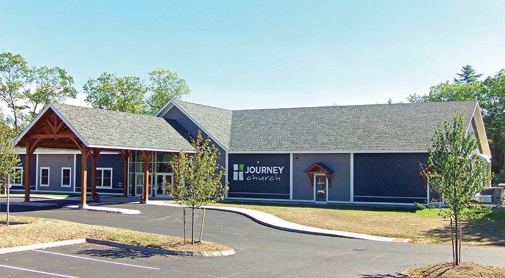 Single-story brick building with a red entrance, gray roof, and landscaped front parking area