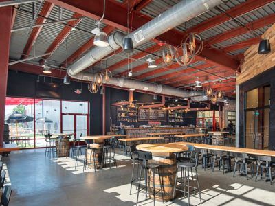 Modern industrial brewery taproom with long wooden tables, metal stools, and large windows
