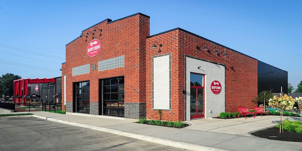 Red brick restaurant building with large windows and red signage on a sunny street corner