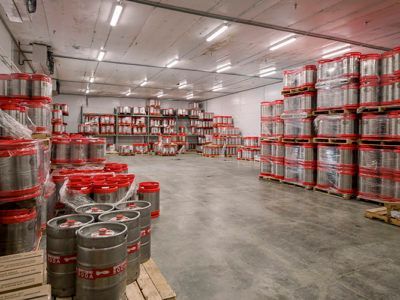 Warehouse with rows of stacked silver kegs with red tops along a wide concrete floor