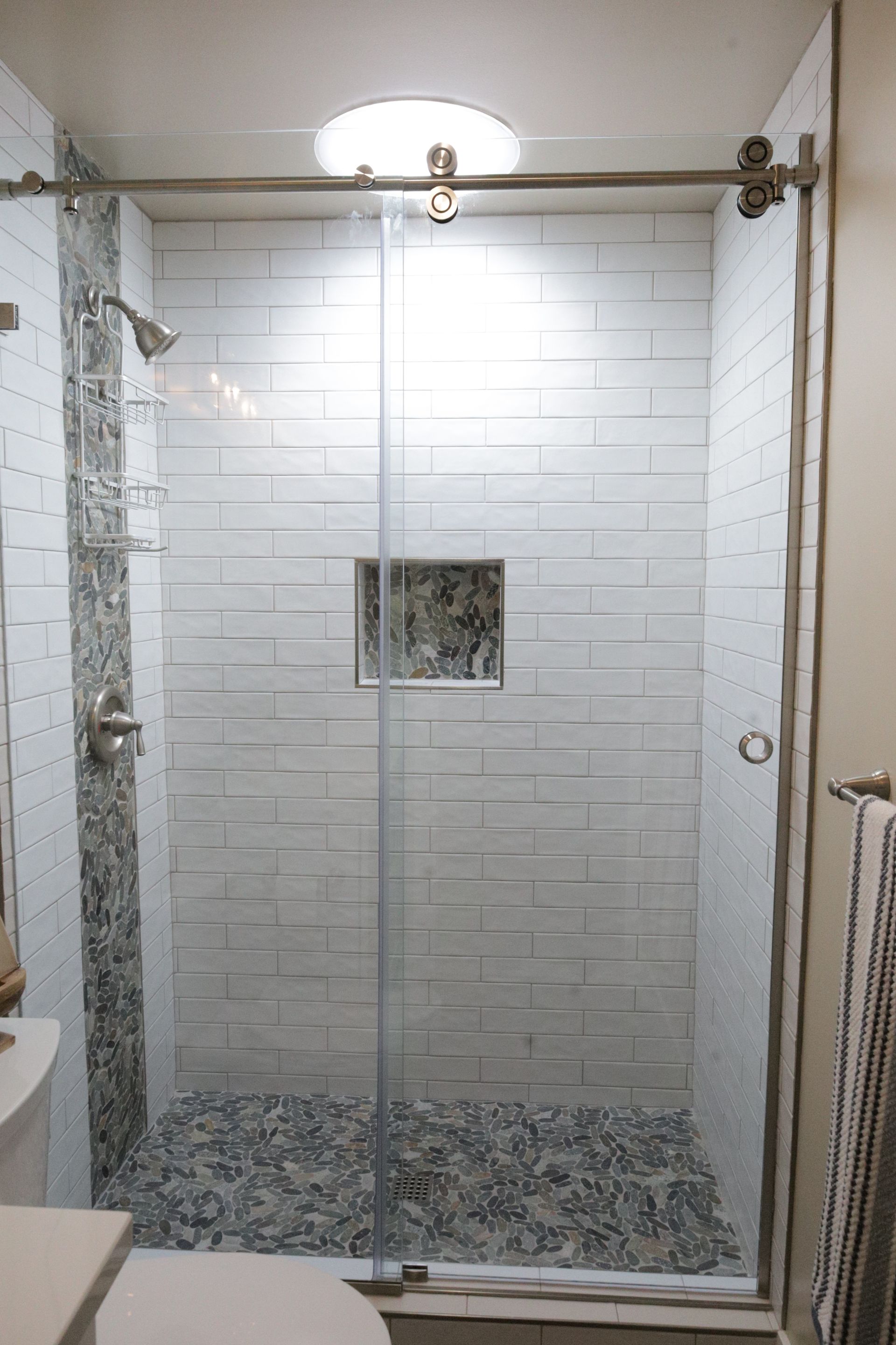 Glass shower stall with white subway tile walls and pebble tile floor in a bathroom