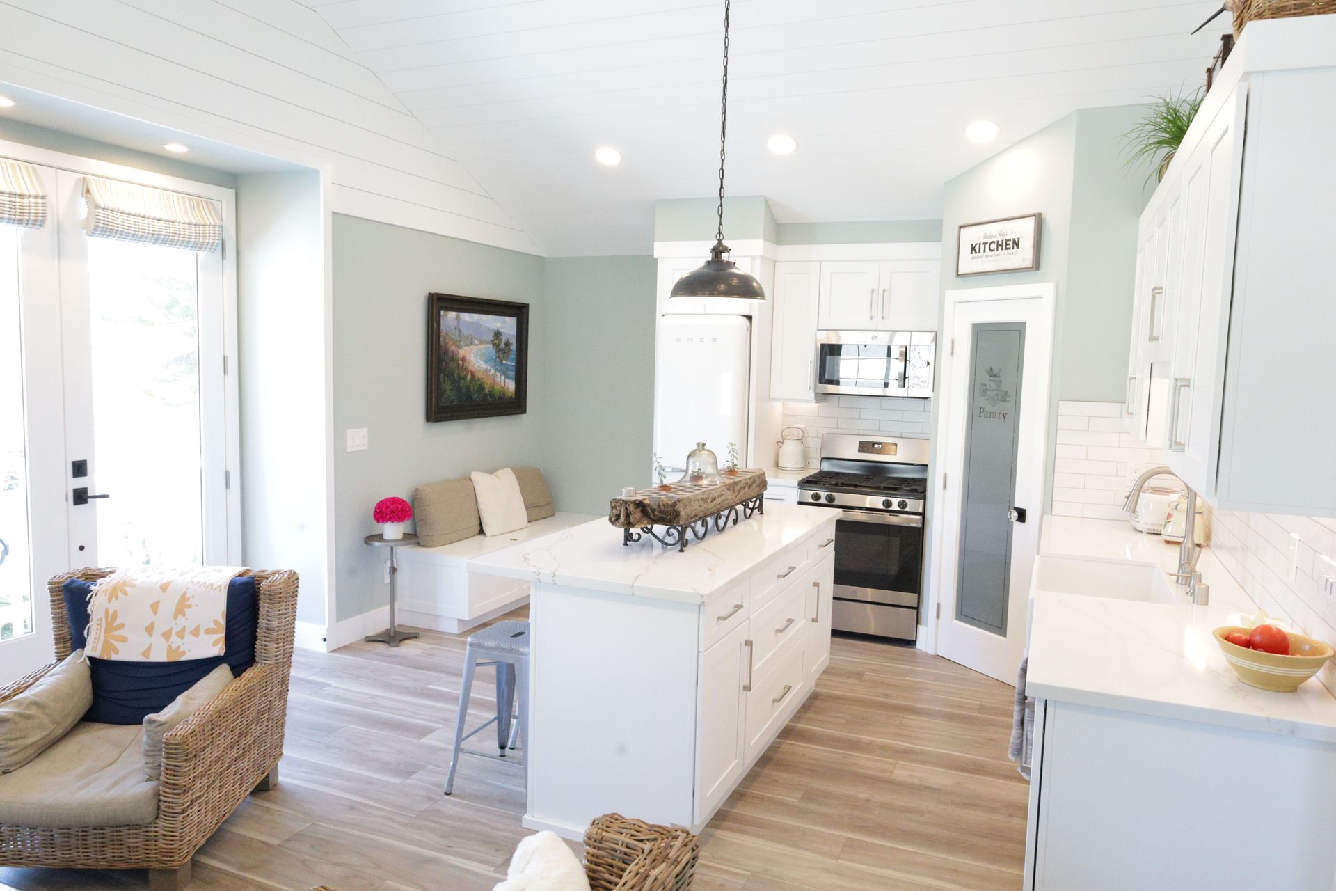 Bright white kitchen with island, hanging pendant light, and wicker chairs in a cozy open-plan room