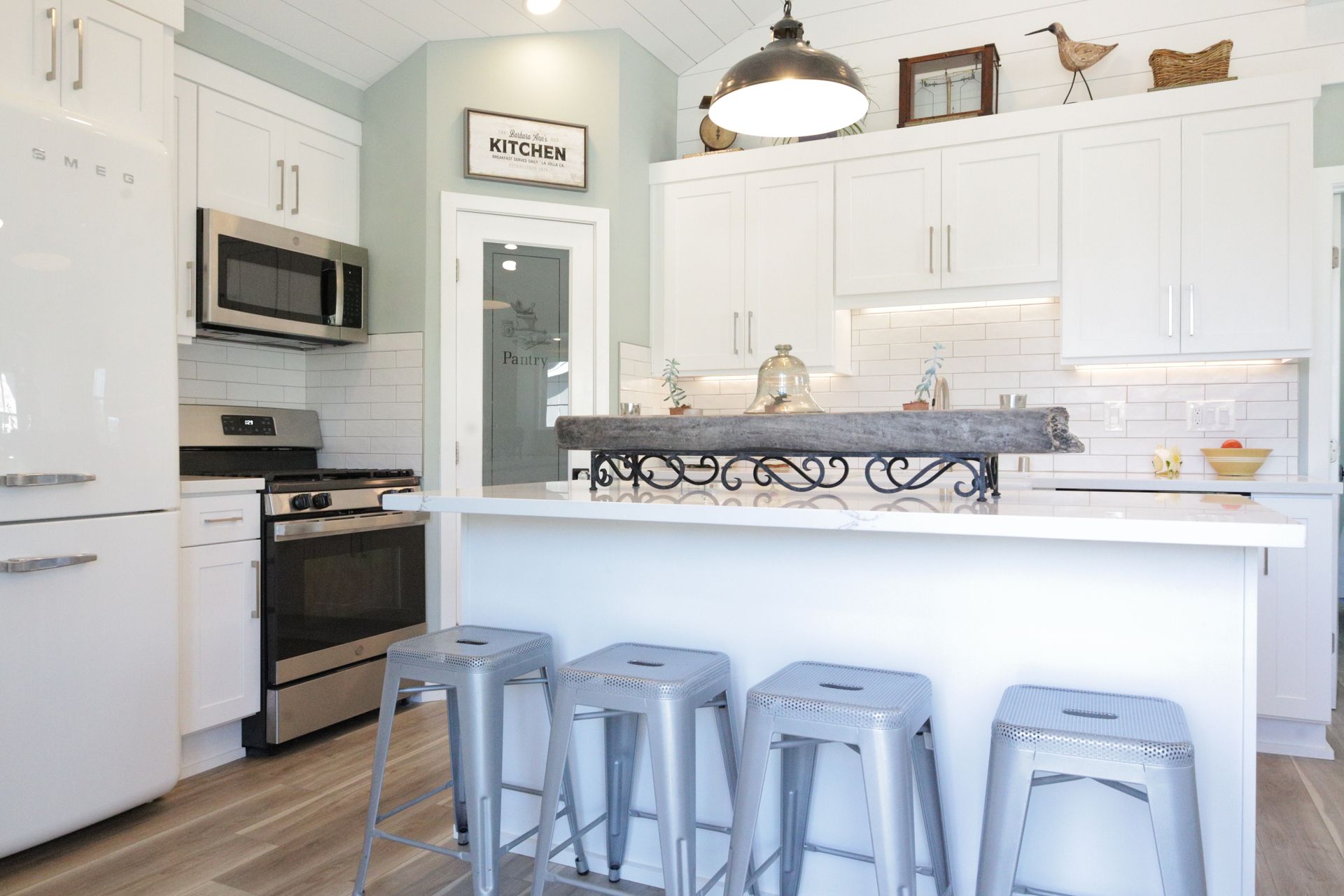 Bright white kitchen with island, gray stools, stainless appliances, and black lantern light fixture