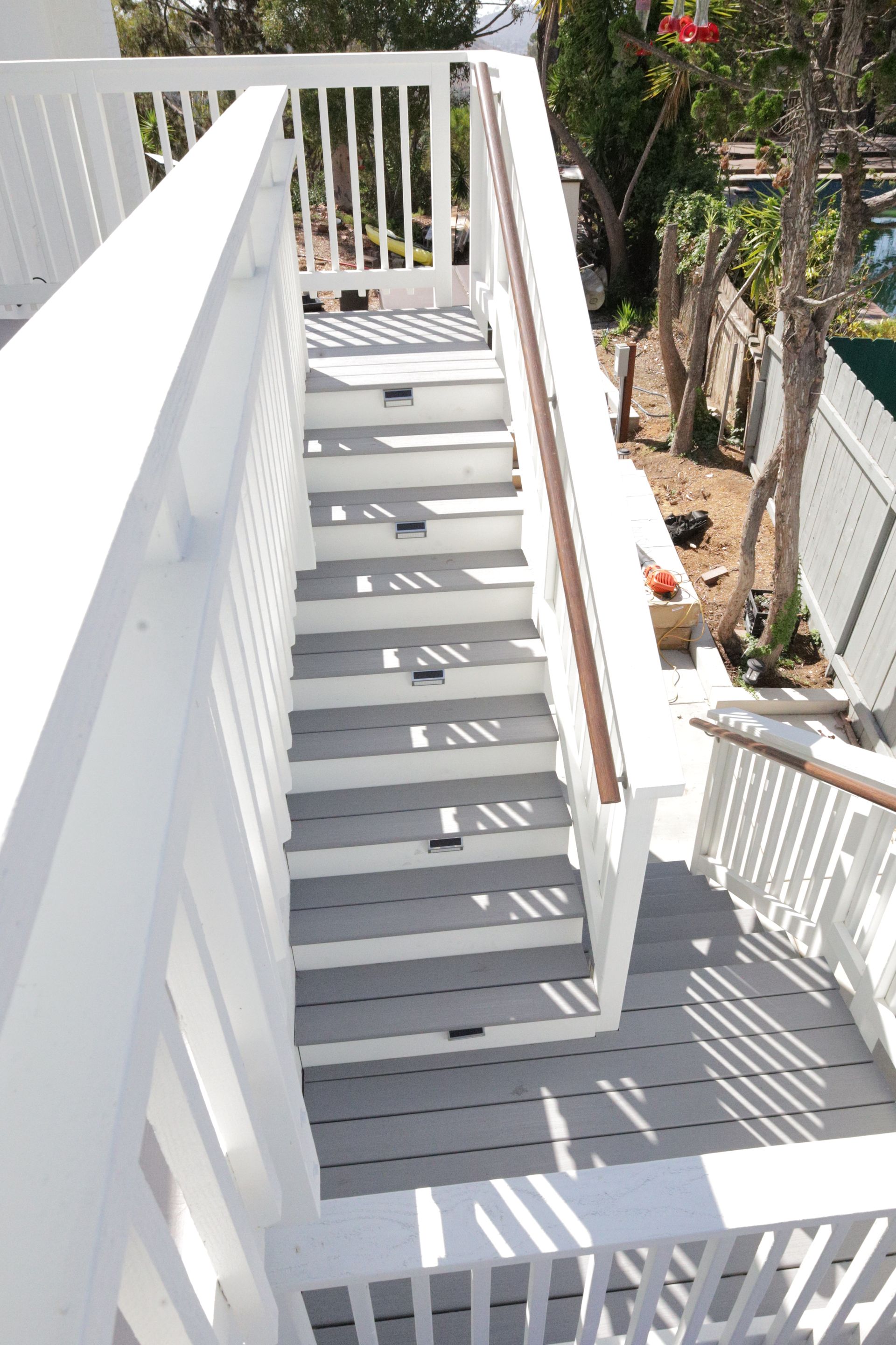 White exterior staircase with railings and shadows, leading down beside a house and tropical plants