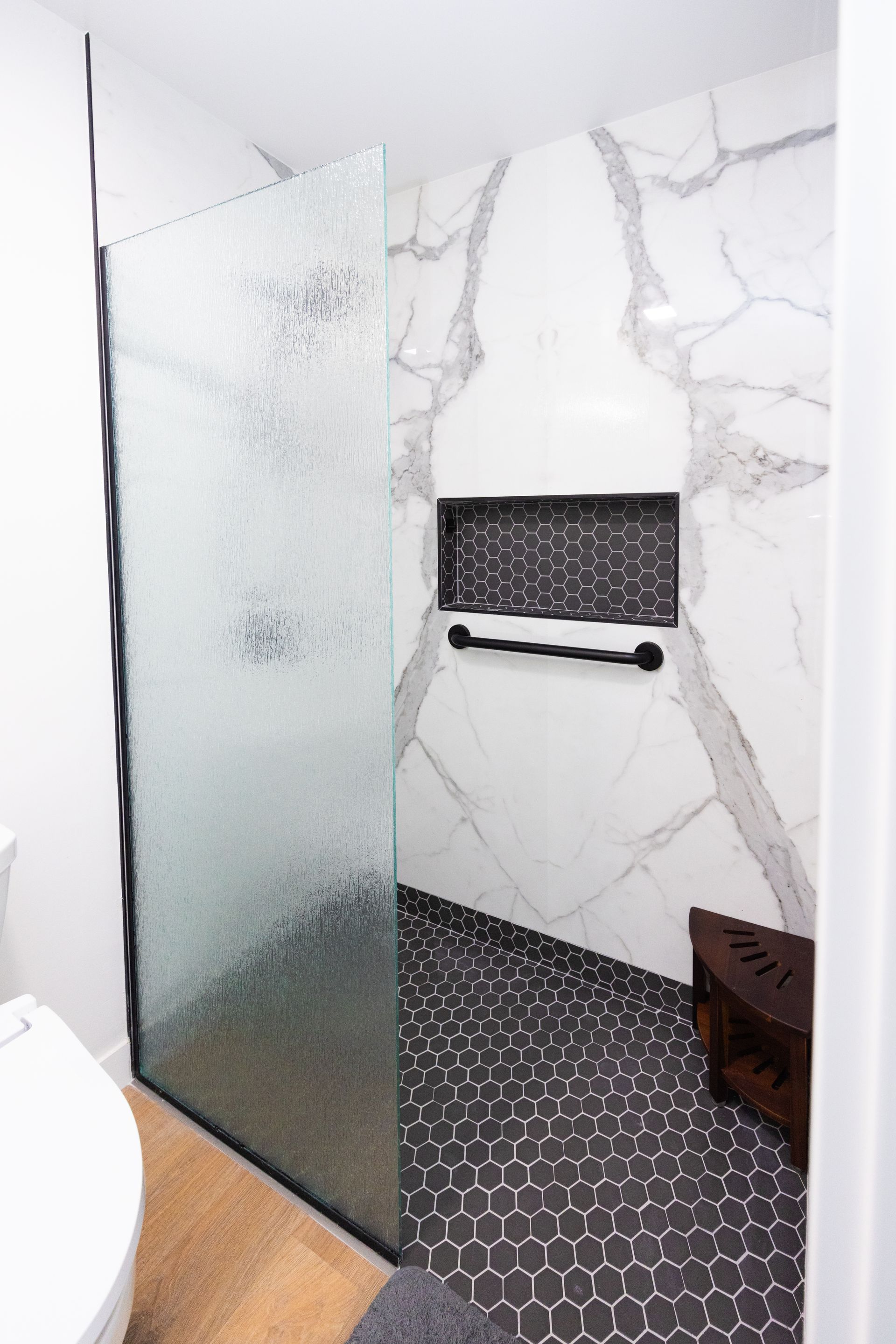 Modern shower with frosted glass, marble-look walls, black hex tile floor, and grab bar.