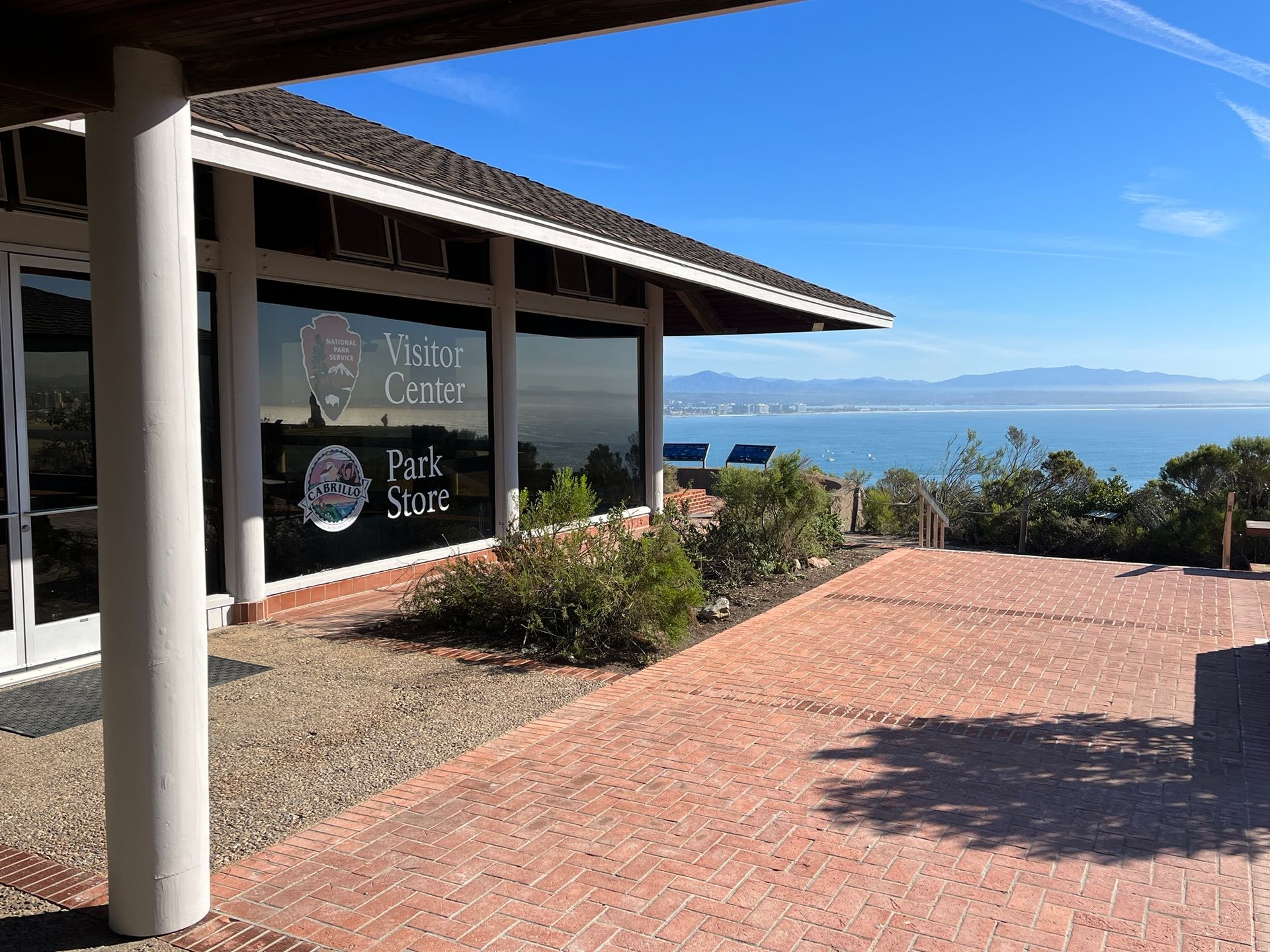 Outdoor terrace with brick paving, shaded building, and ocean view under a clear blue sky