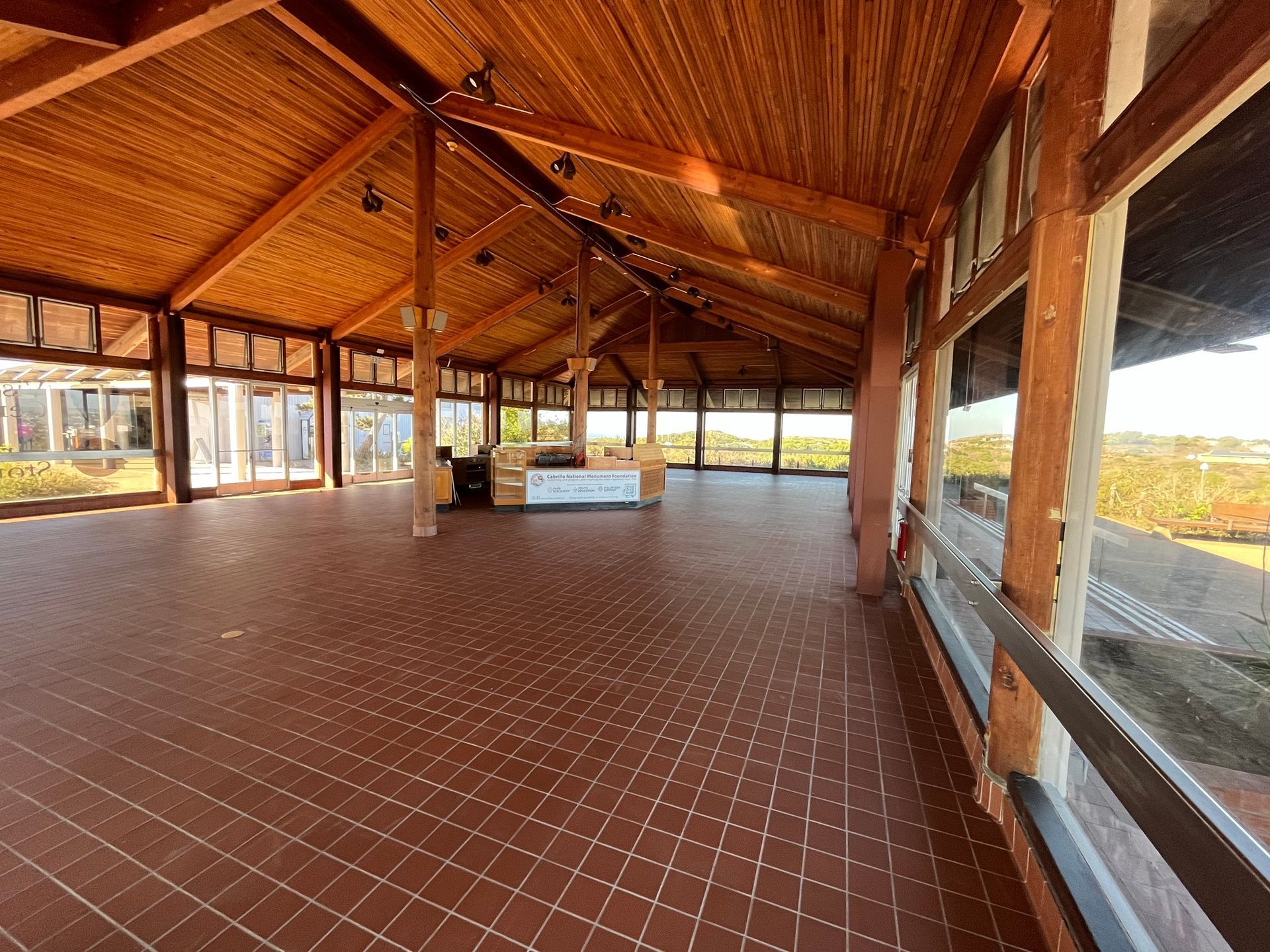Open-air wooden pavilion with tiled floor, sloped roof, and panoramic windows overlooking fields