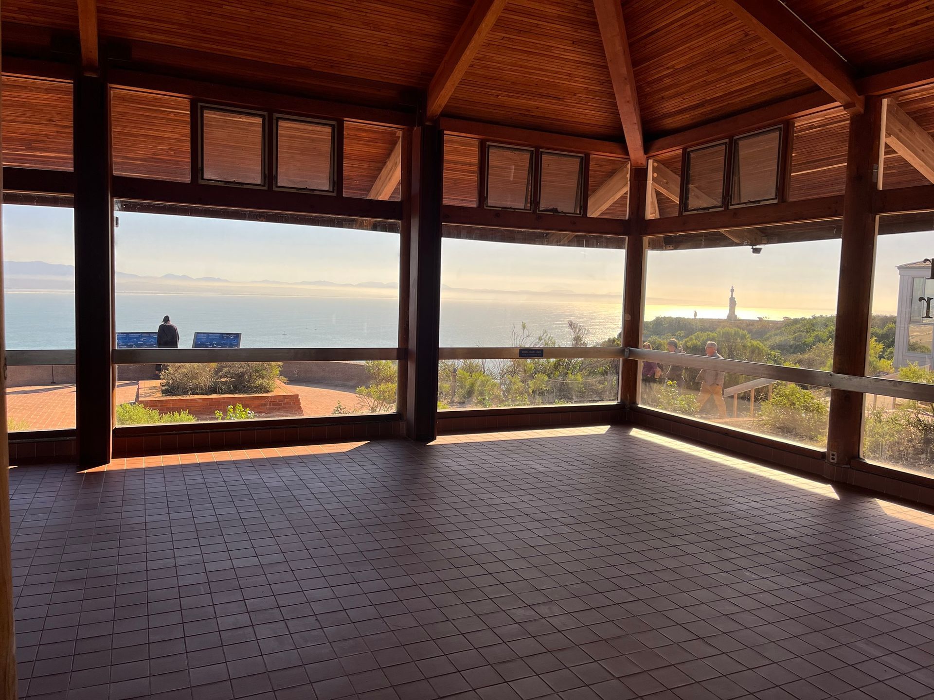 Wooden open-air pavilion at sunset with ocean view and distant tower