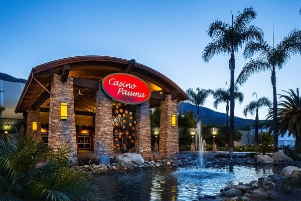 Canoe Restaurant entrance at dusk, with stone facade, red sign, palm trees, and reflecting pond
