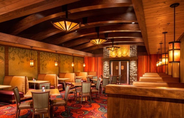 Warm, empty restaurant dining room with wooden beams, red patterned carpet, and softly lit tables