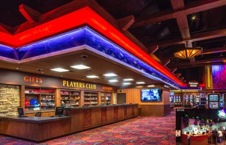 Casino sportsbook lounge with red and blue neon lighting, wooden bar, and multiple TV screens