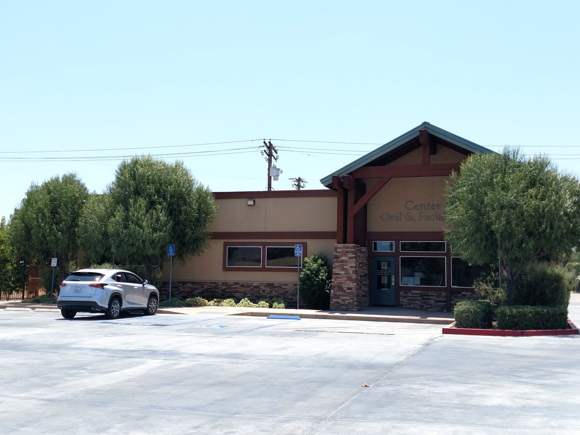 Small tan building with a covered entrance and parked white SUV in front under a clear sky