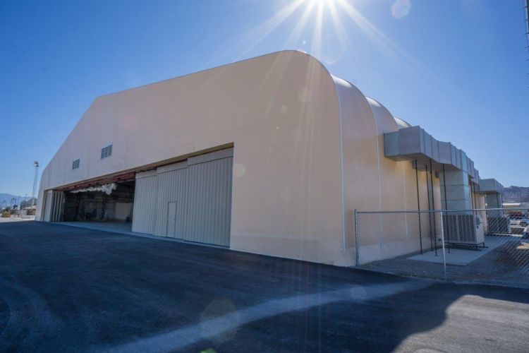 Large beige warehouse building with loading doors on an empty industrial street under bright sun
