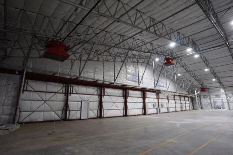 Empty warehouse interior with high arched ceiling, bright lights, and concrete floor