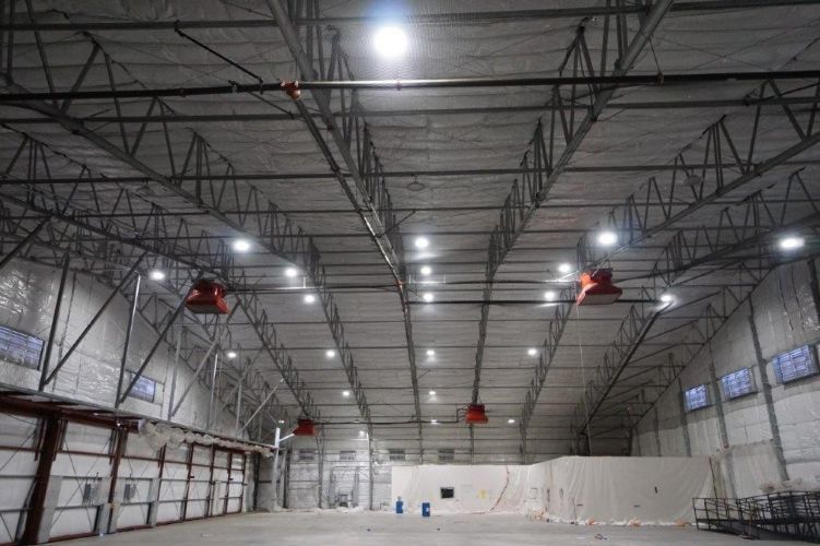 Large indoor warehouse with high ceiling, white walls, hanging lights, and a few red lifts or equipment units