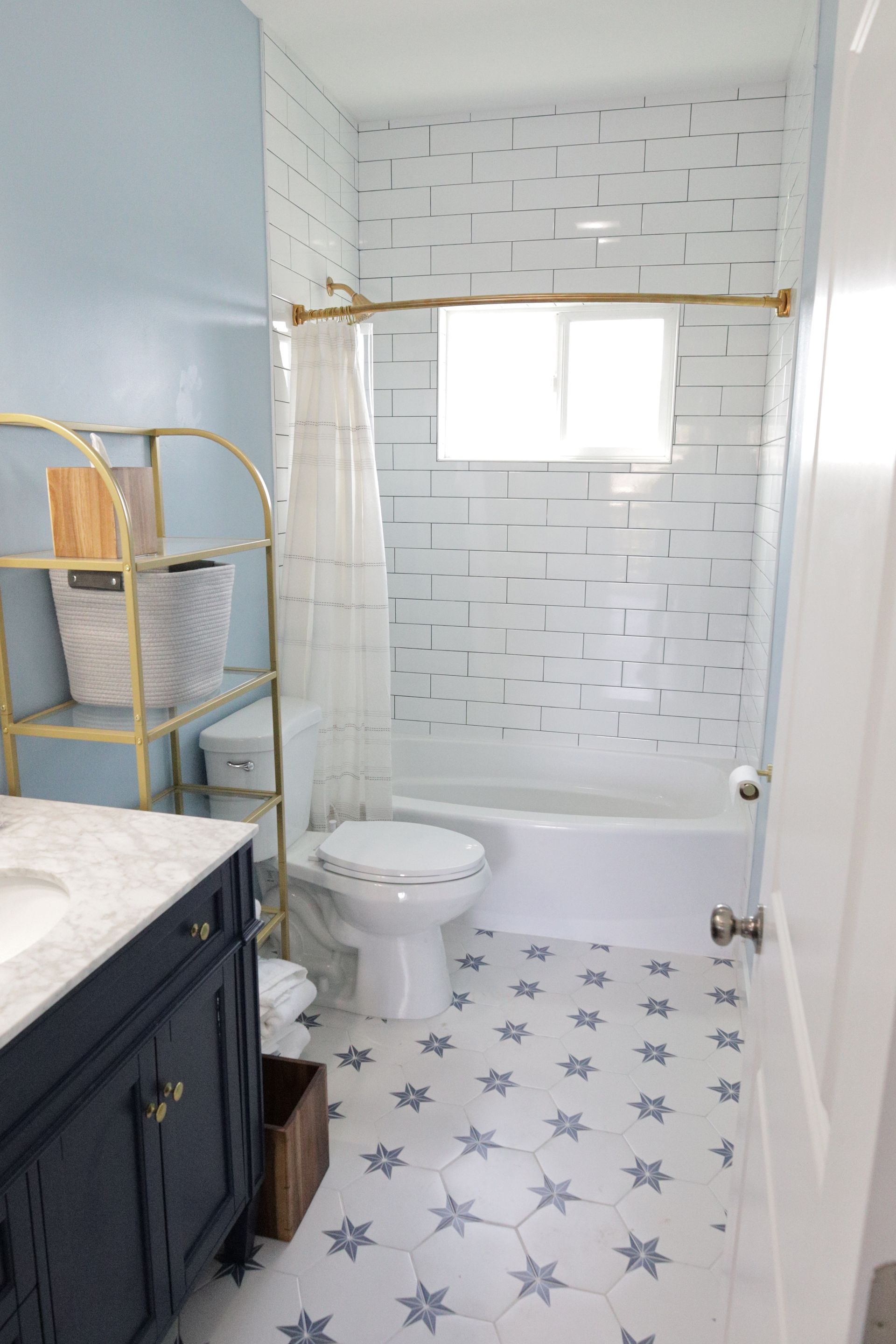 Small bathroom with white tile shower, toilet, and vanity with navy cabinet and light wood shelving.