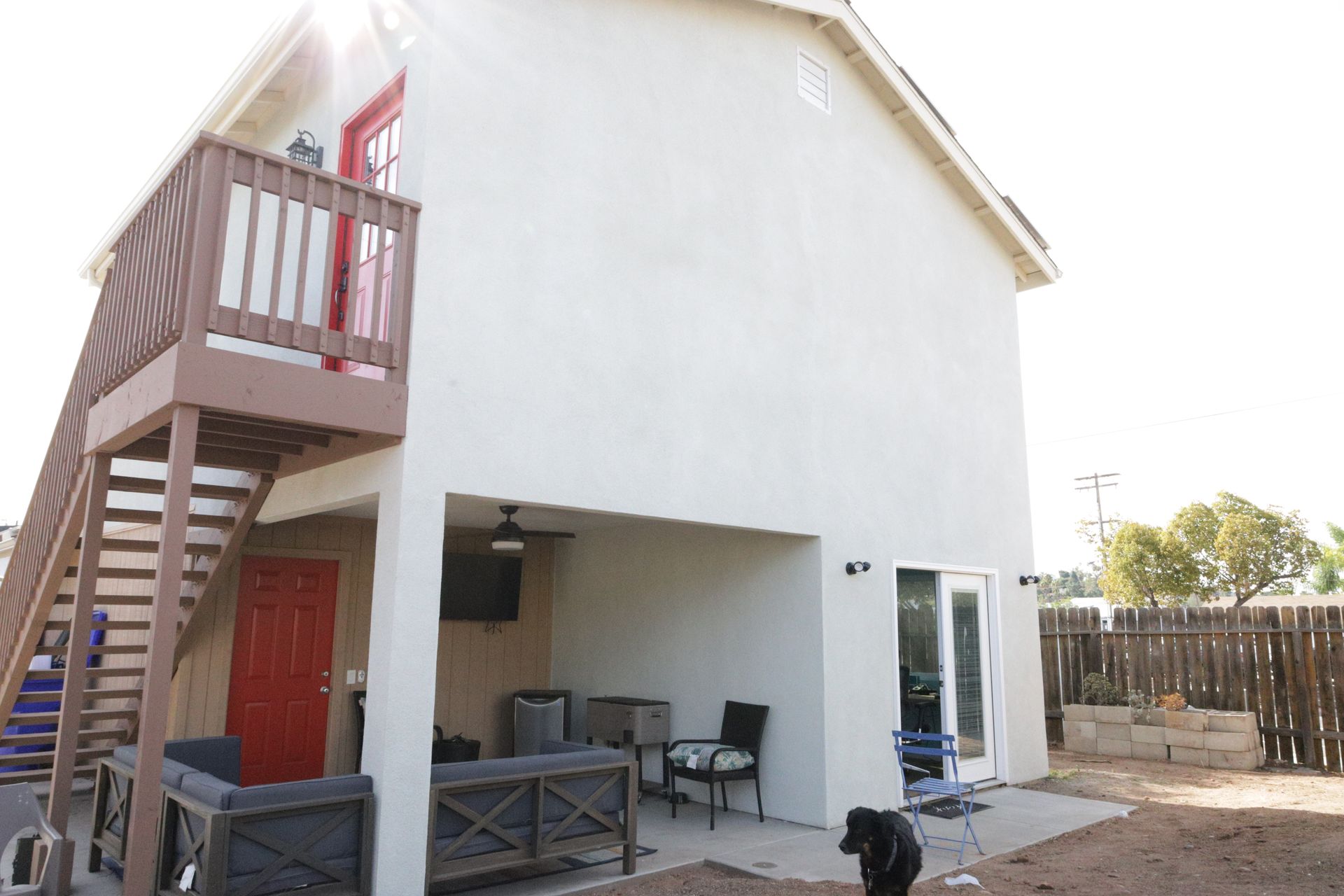 Two-story house with exterior stairs, a small balcony, and a patio with outdoor furniture.